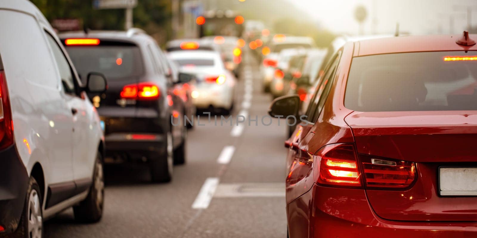 Rear view of modern car with brake lights on during rush hour. Concept of irritation of being delayed by traffic jam. Road full of vehicles in panoramic composition.