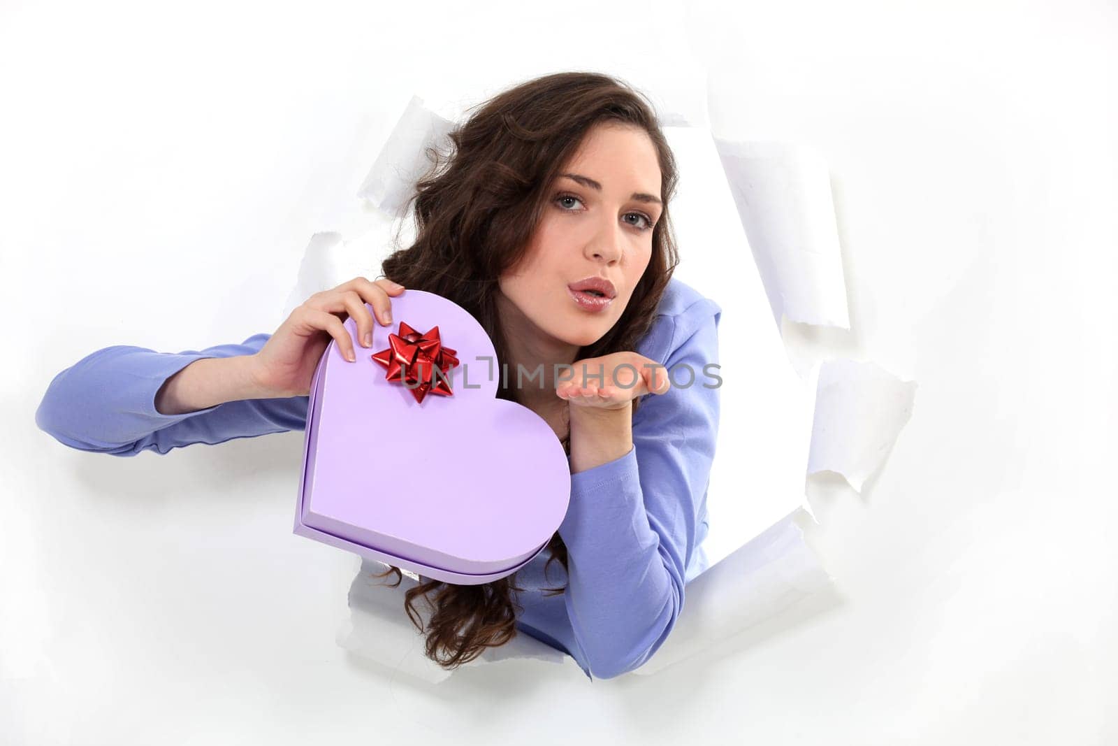 brunette holds box in shape of heart blowing a kiss