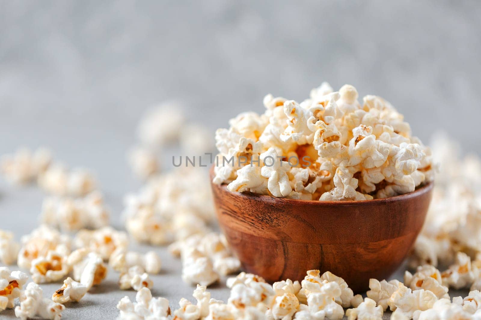 A wooden bowl of salted popcorn on rustic grey table. Selective focus and copyspace for text. Concept of relax and time off.