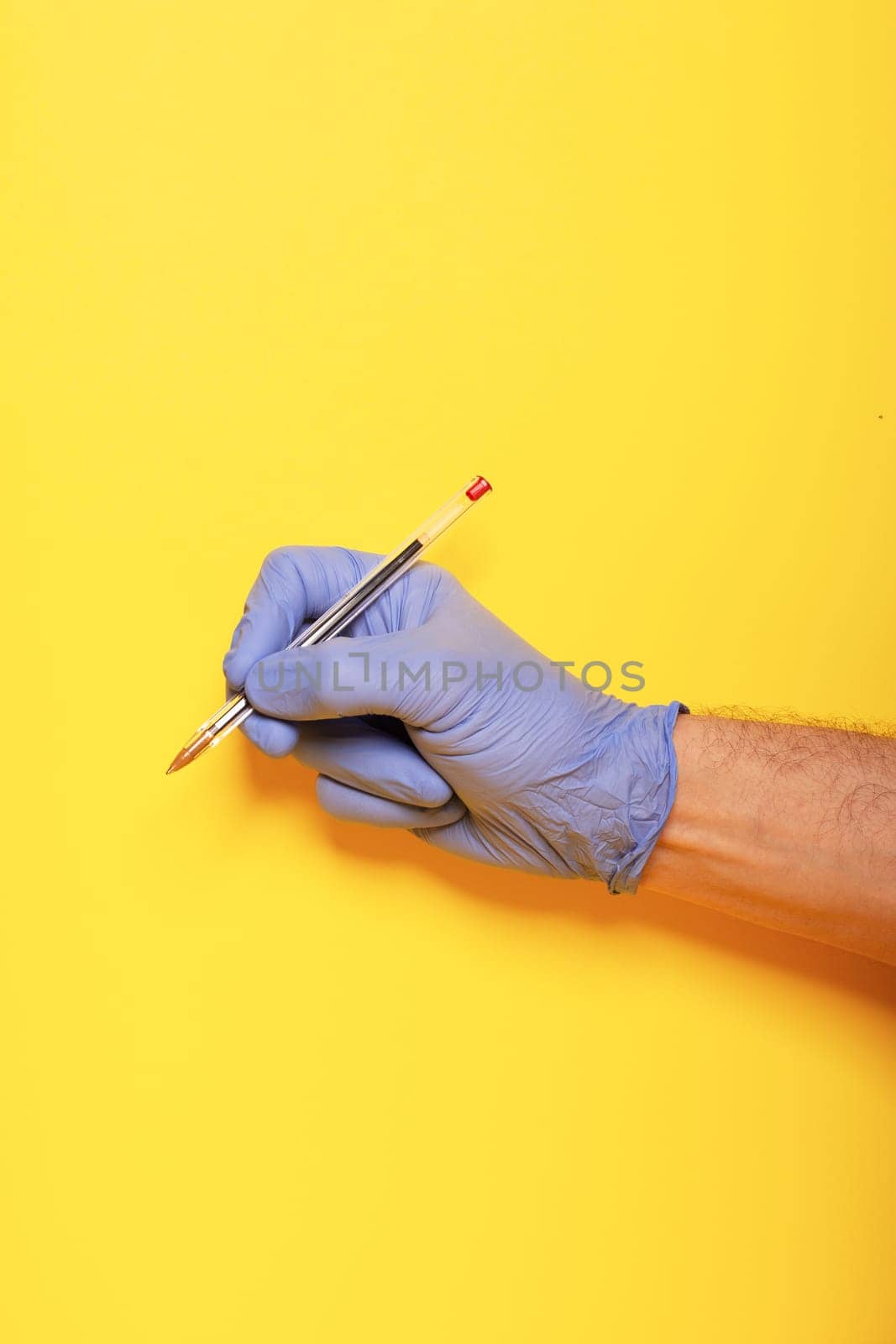 Hands gestures. human hand in latex glove writes with the red ballpoint pen isolated on yellow background with copy space