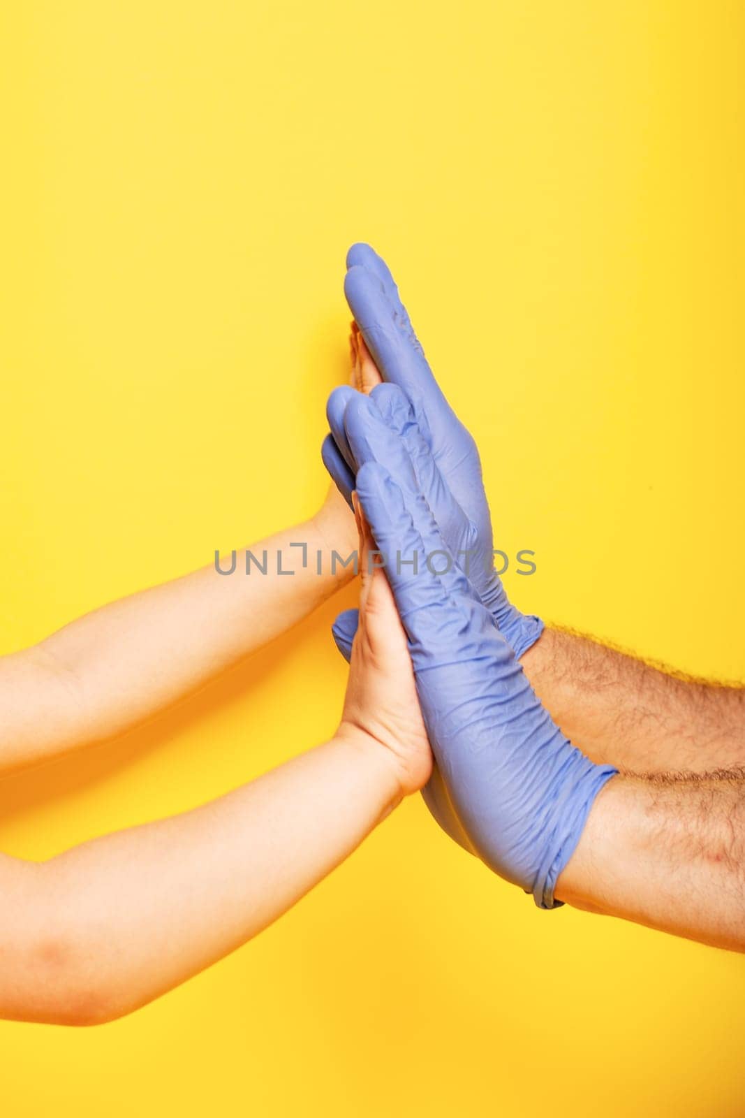 Hands gestures. the palms of the child and the father against each other as a sign of agreement, in latex glove over yellow background. Vertical orientation