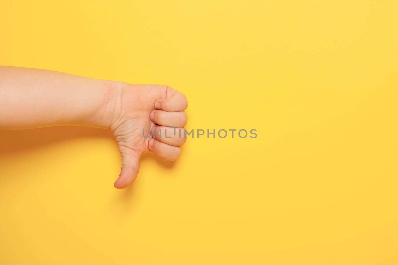 Hands gestures. Baby hand showing symbol of disagreement isolated on yellow background with copy space