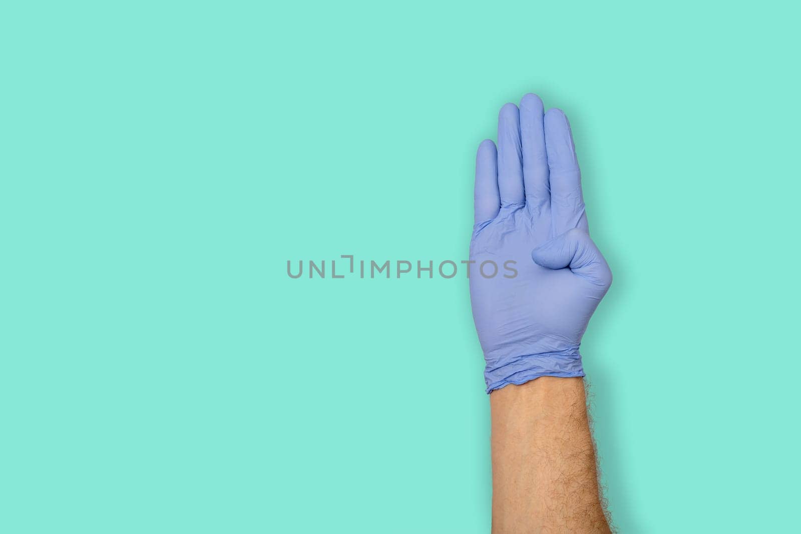Hands gestures. human hand in latex glove with palm up and thumb finger bent isolated on green pastel background with copy space.