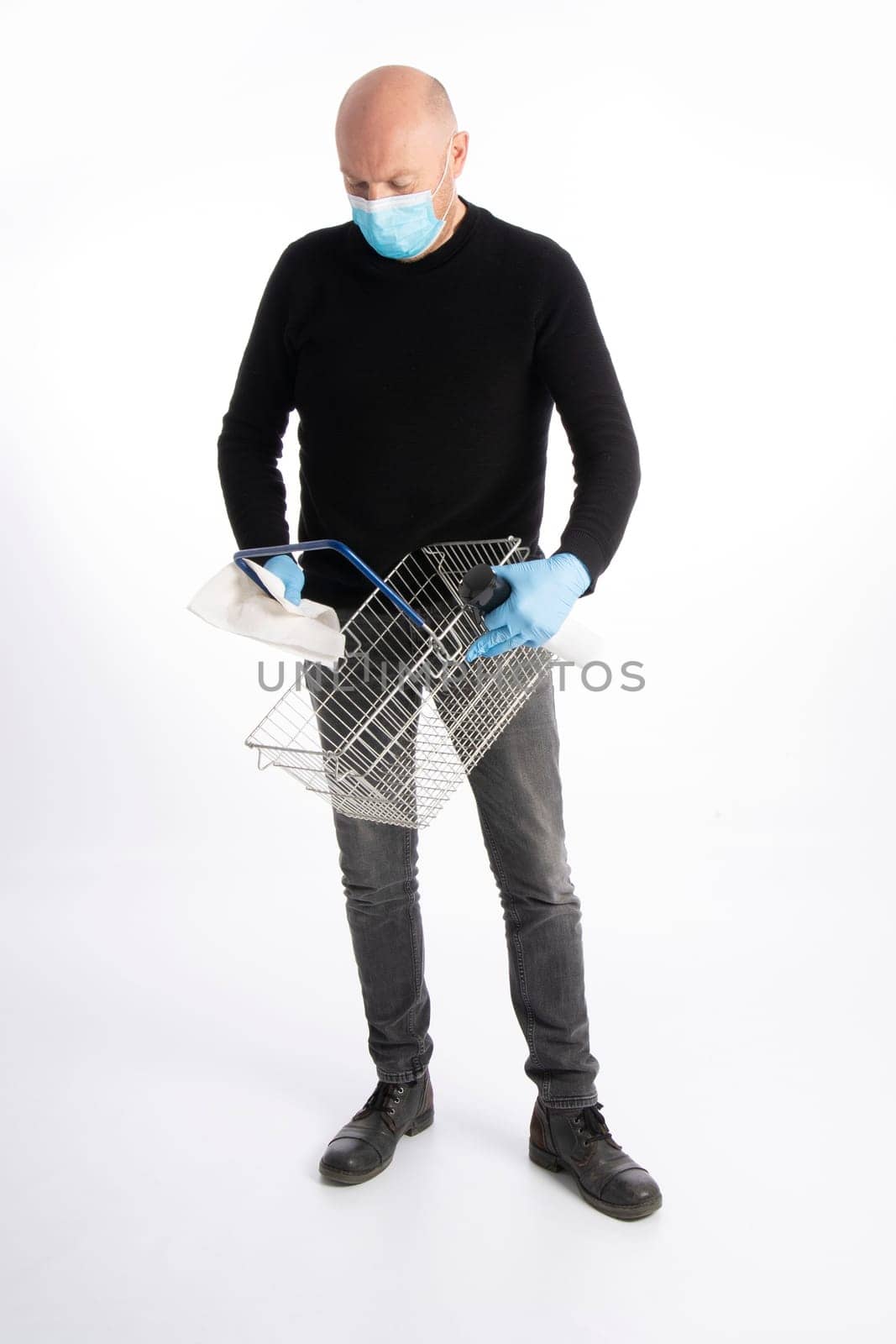Man with mouth protection and hand gloves cleaning a shopping basket, isolated on white background
