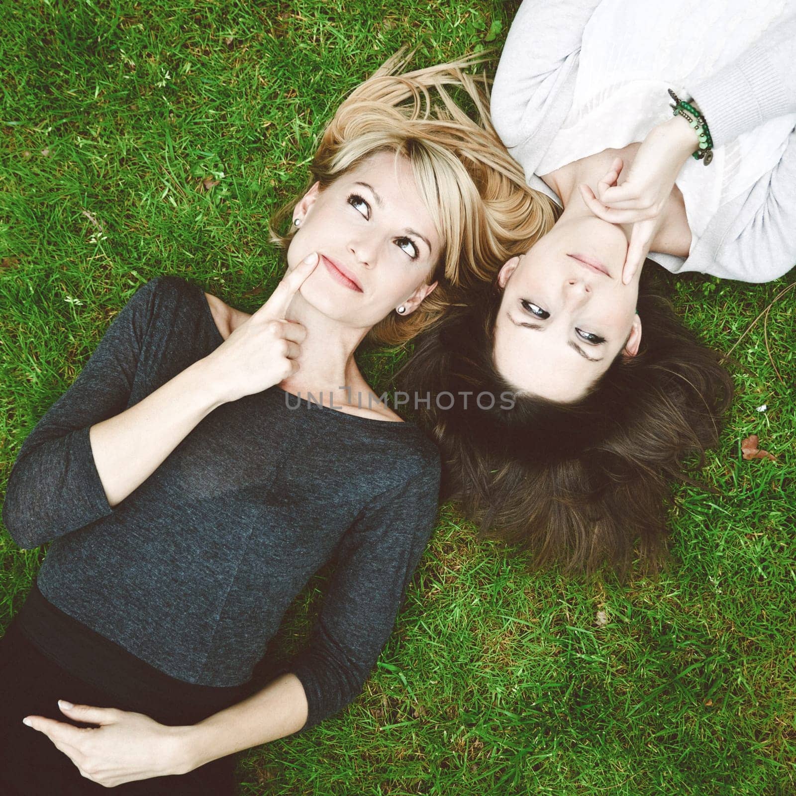 Two thoughtful girls lying in the grass have an smart idea.