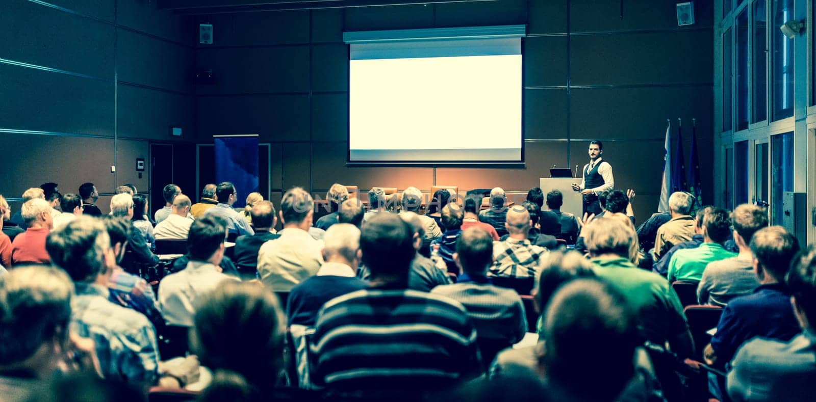 Speaker giving a talk in conference hall at business meeting event. Rear view of unrecognizable people in audience at the conference hall. Business and entrepreneurship concept.