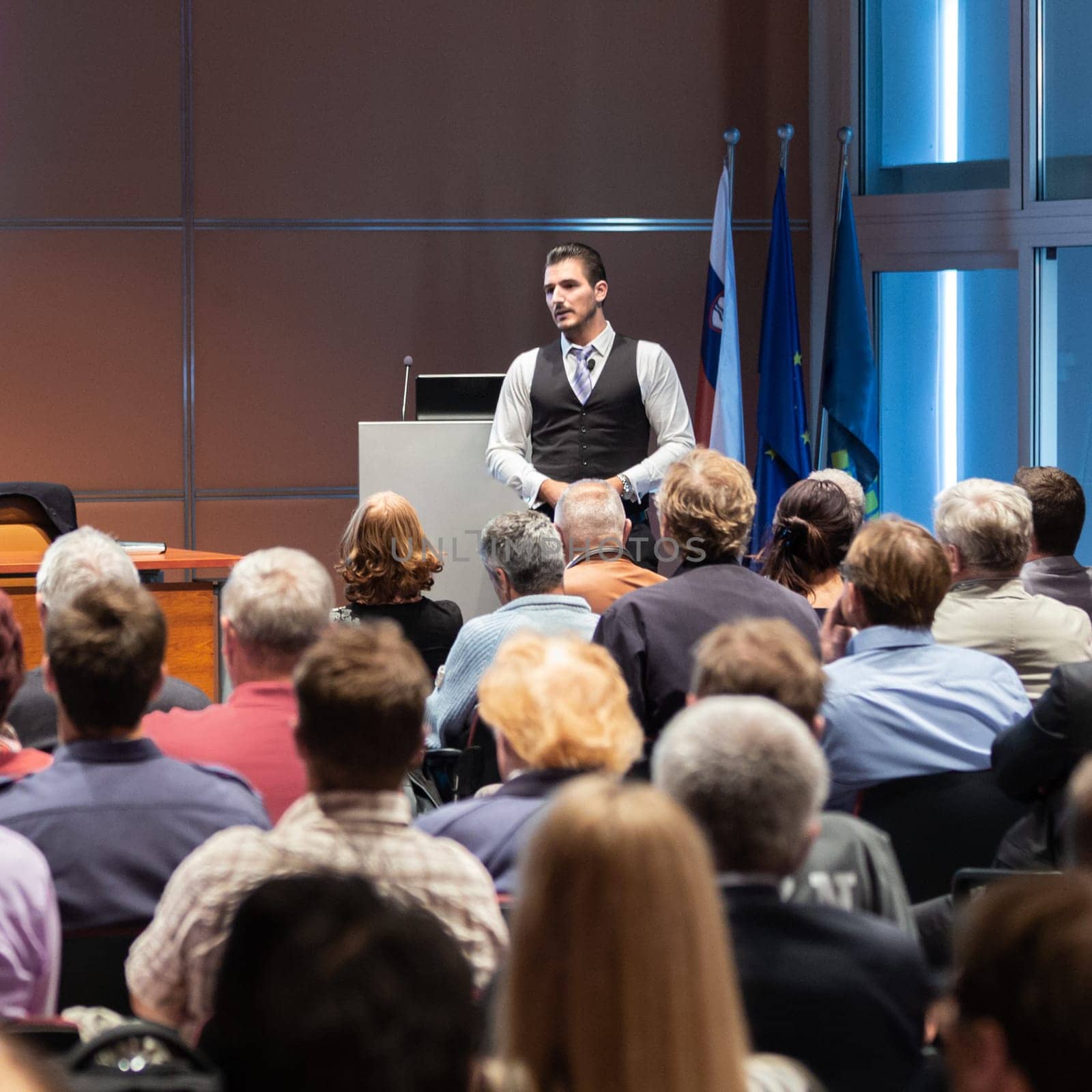 Speaker giving a talk in conference hall at business meeting event. Rear view of unrecognizable people in audience at the conference hall. Business and entrepreneurship concept.