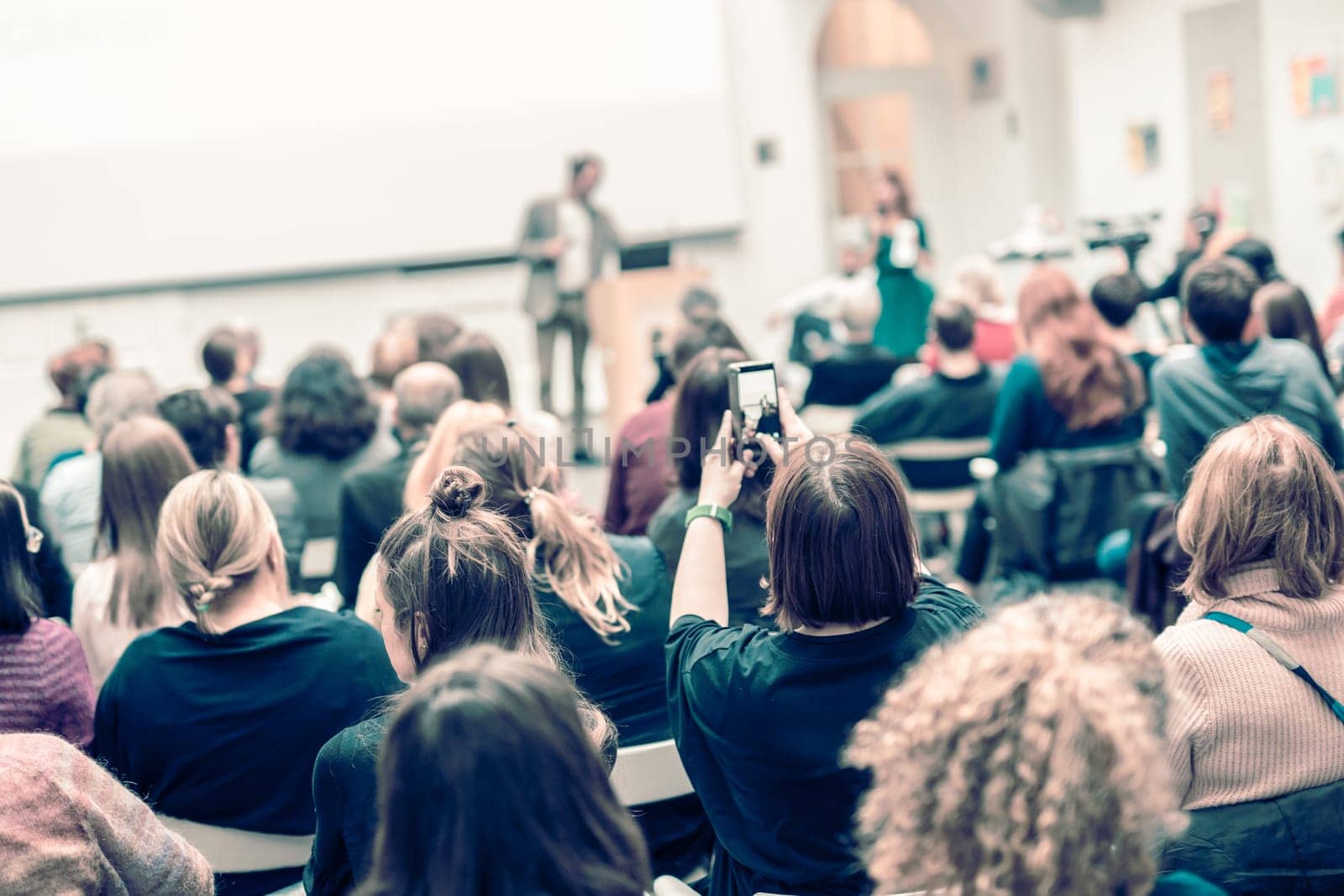 Male speaker giving presentation in lecture hall at university workshop. Audience in conference hall. Rear view of unrecognized participant in audience. Scientific conference event.