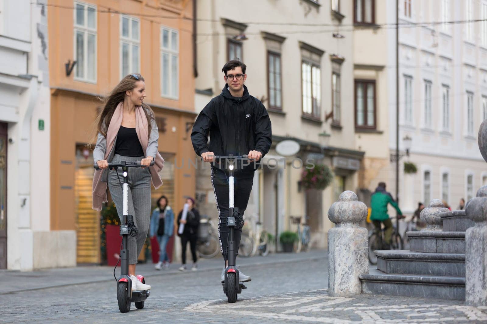 Trendy fashinable teenagers riding public rental electric scooters in urban city environment. New eco-friendly modern public city transport in Ljubljana, Slovenia.