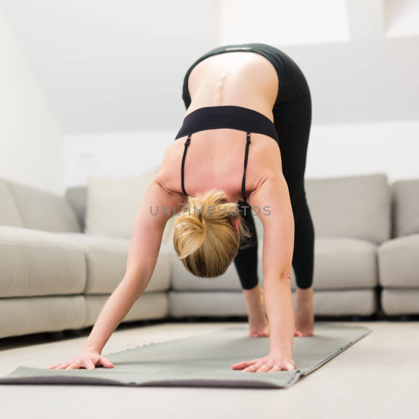 Beautiful blonde woman doing home workout indoors. Woman practice yoga at home. Fit girl using workout tutorials for healthy active lifestyle. Woman using quarantine for home workouts. Stretching