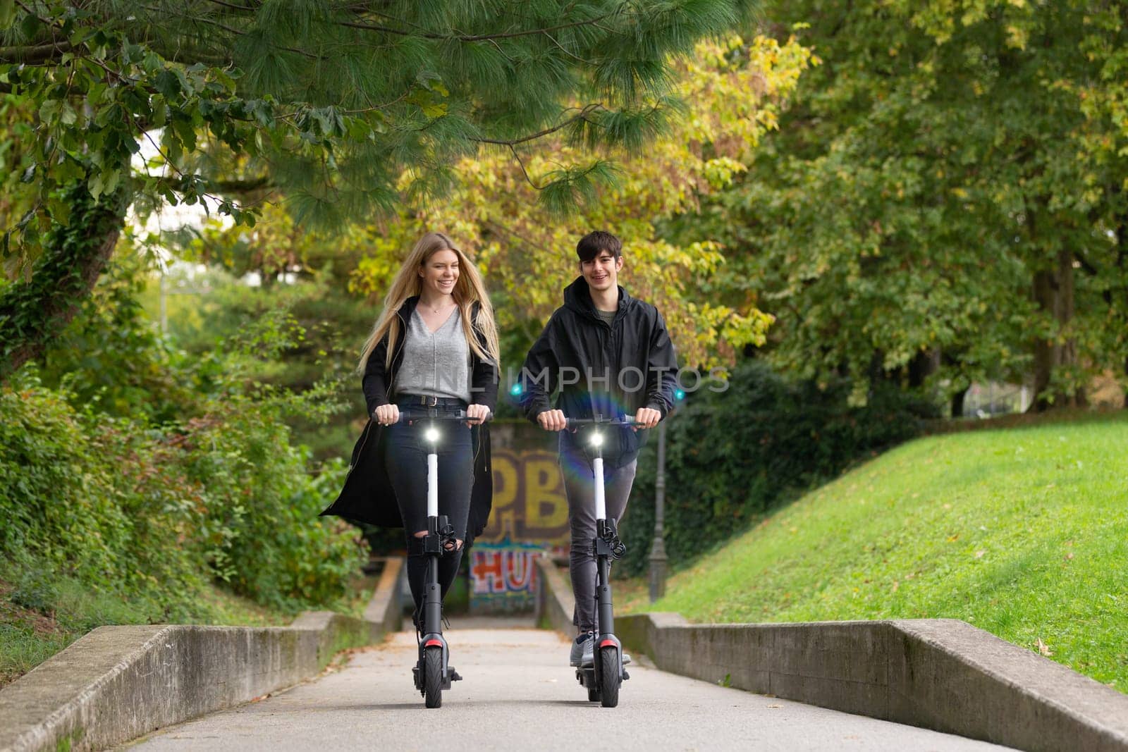 Trendy fashinable teenagers riding public rental electric scooters in urban city park. New eco-friendly modern public city transport in Ljubljana, Slovenia.