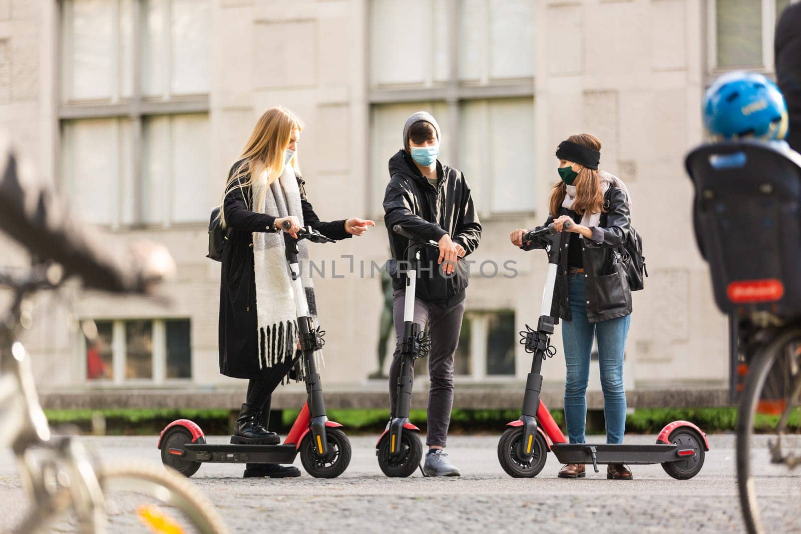 Trendy fashinable group of friends riding public rental electric scooters in urban city environment at fall. New eco-friendly modern public city transport in Ljubljana, Slovenia.