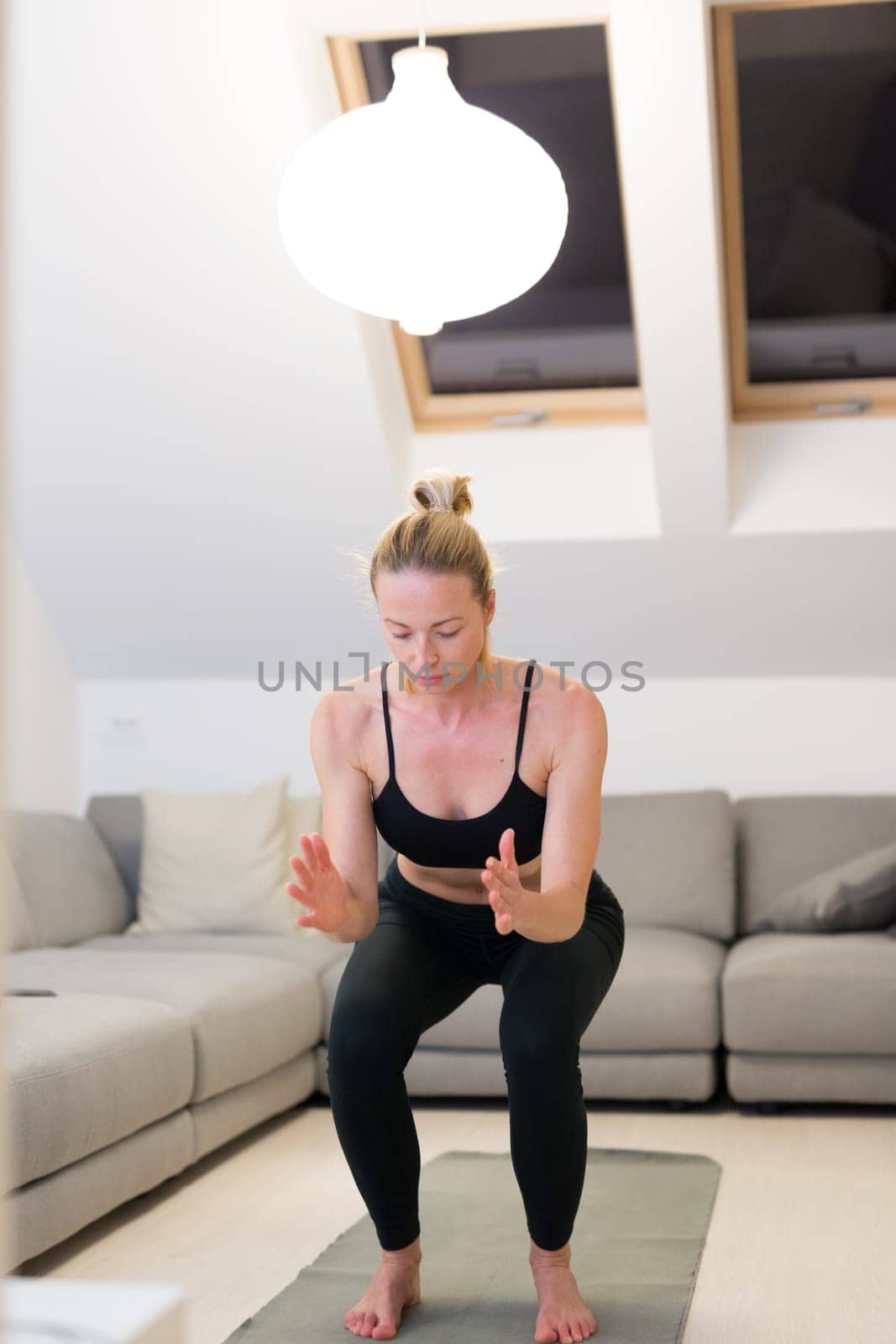 Beautiful blonde woman doing home workout indoors. Woman practice yoga at home. Fit girl using workout tutorials for healthy active lifestyle. Woman using quarantine for home workouts. Stretching