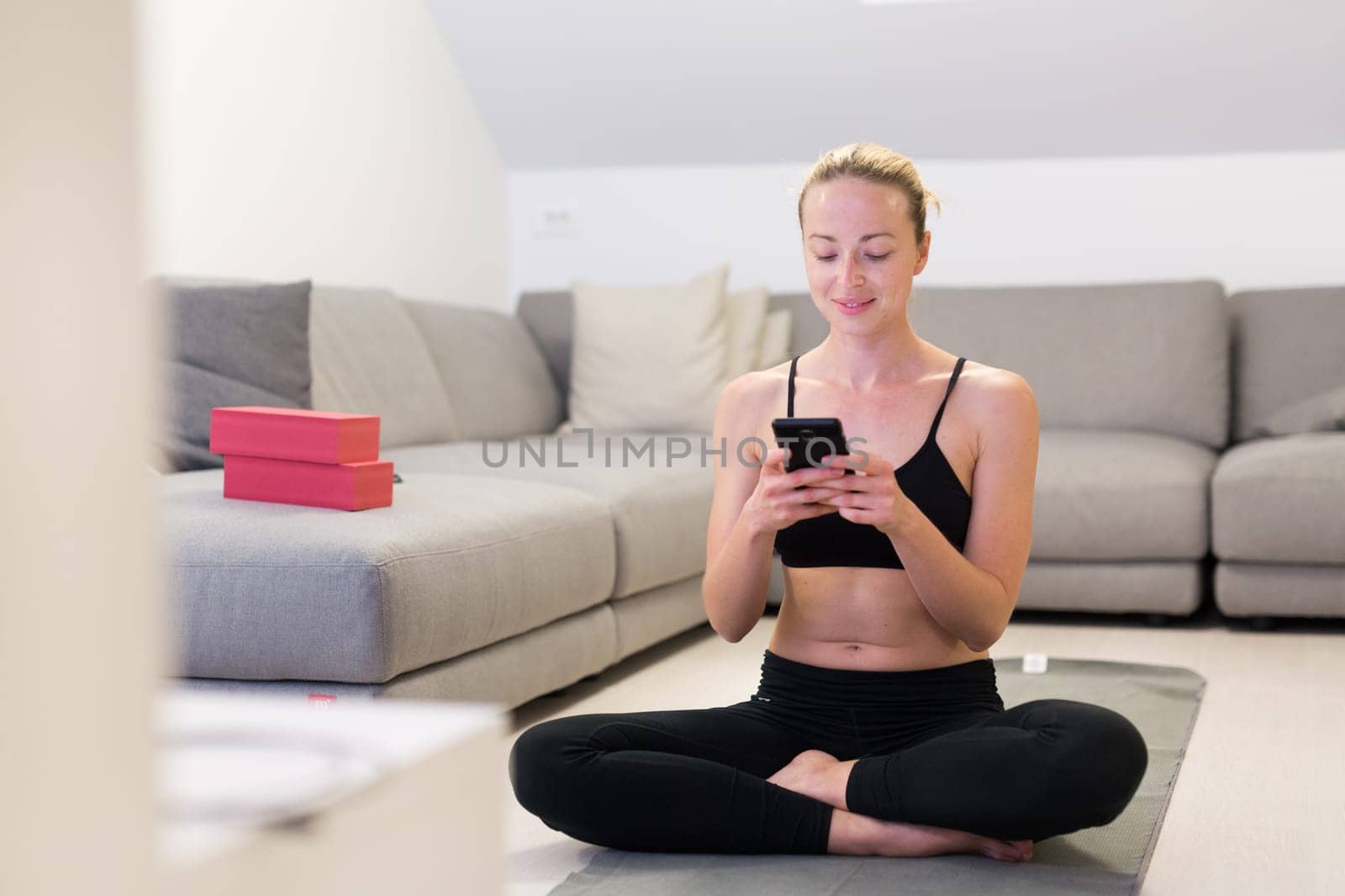 Beautiful blonde woman doing home workout indoors. Woman practice yoga at home. Fit girl using workout tutorials for healthy active lifestyle. Woman using quarantine for home workouts. Stretching