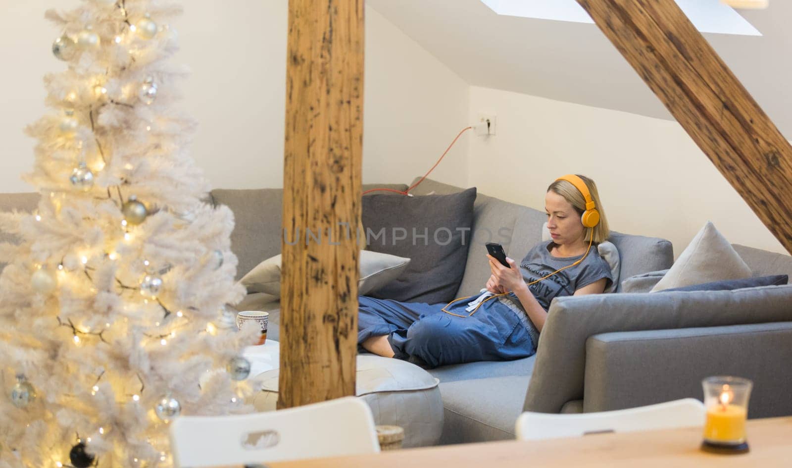 Young thoughtful woman sitting indoors at home living room sofa using social media on phone for video chatting and staying connected with her loved ones. Stay at home, social distancing lifestyle.