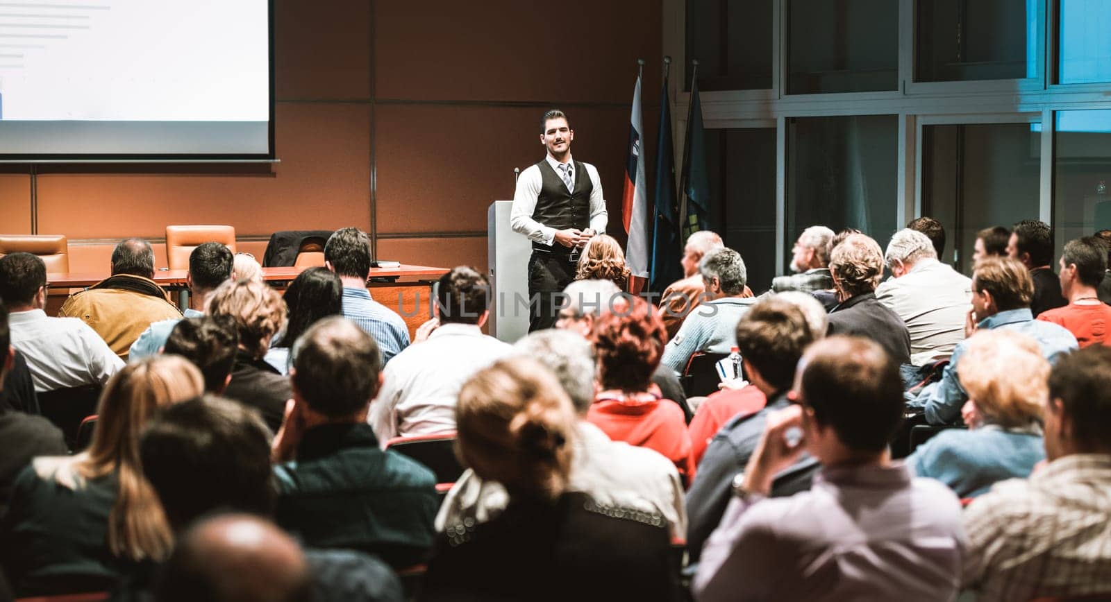 Speaker giving a talk in conference hall at business meeting event. Rear view of unrecognizable people in audience at the conference hall. Business and entrepreneurship concept.