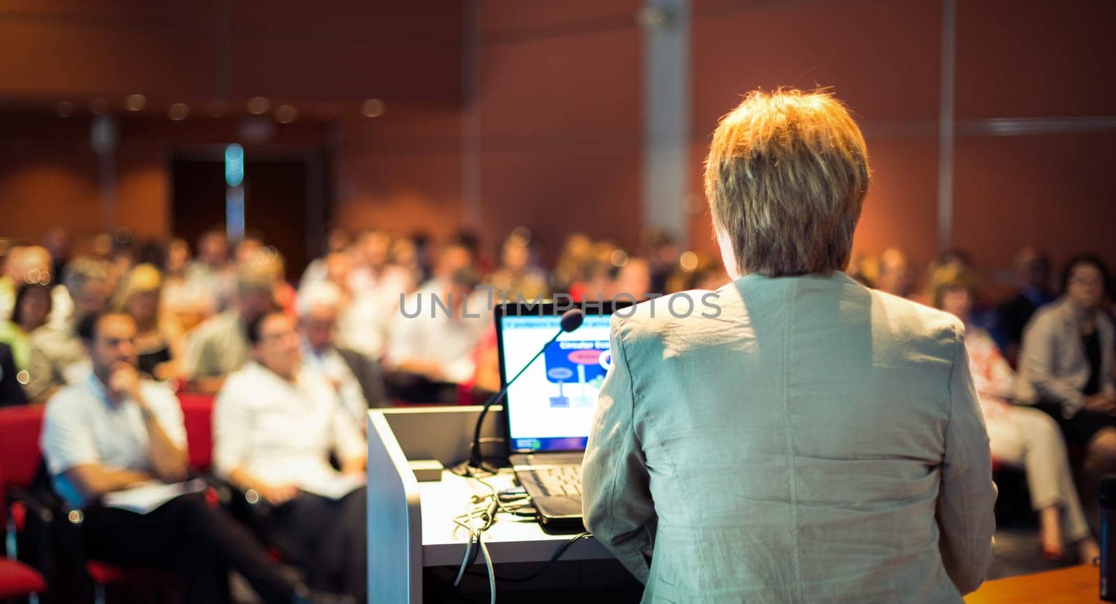 Senior business woman lecturing at Conference. Audience at the lecture hall.