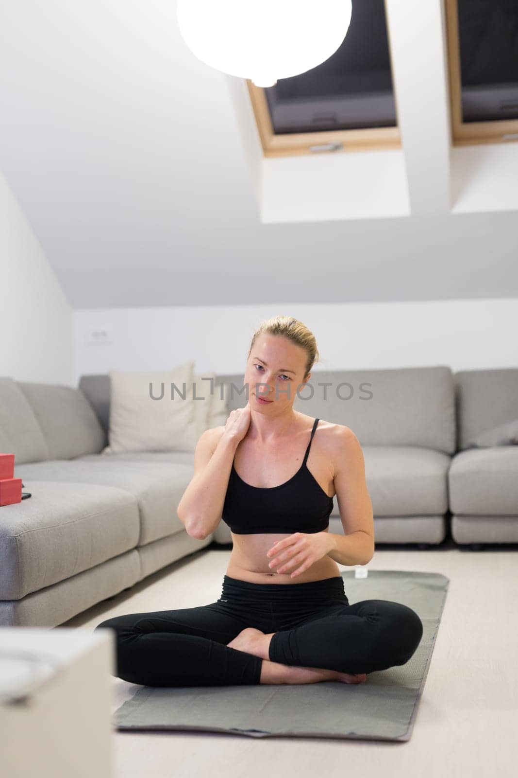 Beautiful blonde woman doing home workout indoors. Woman practice yoga at home. Fit girl using workout tutorials for healthy active lifestyle. Woman using quarantine for home workouts. Stretching