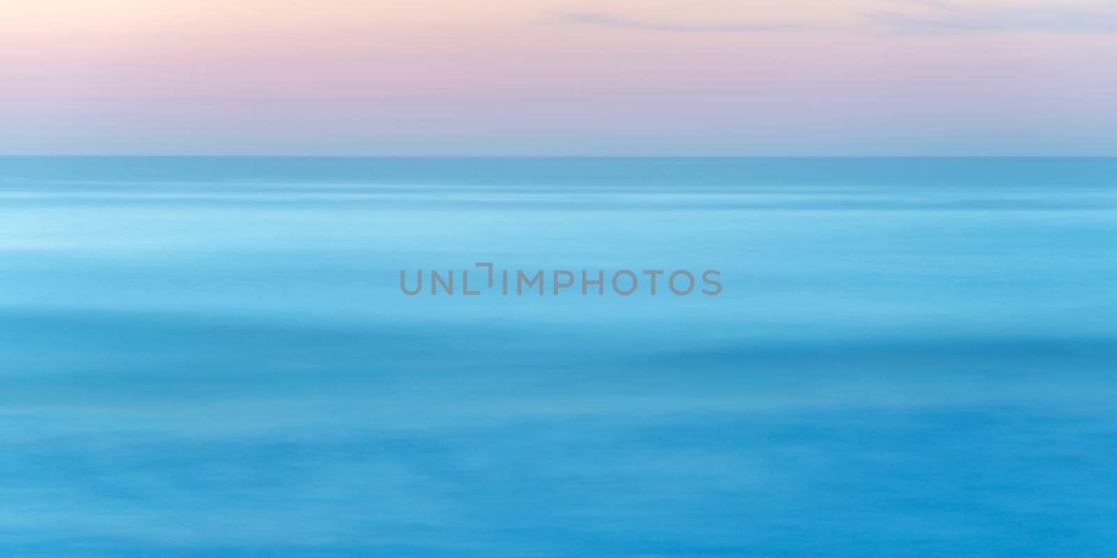 Long exposure of seascape at sunset, blue sea water abstract background, pastel pink sky