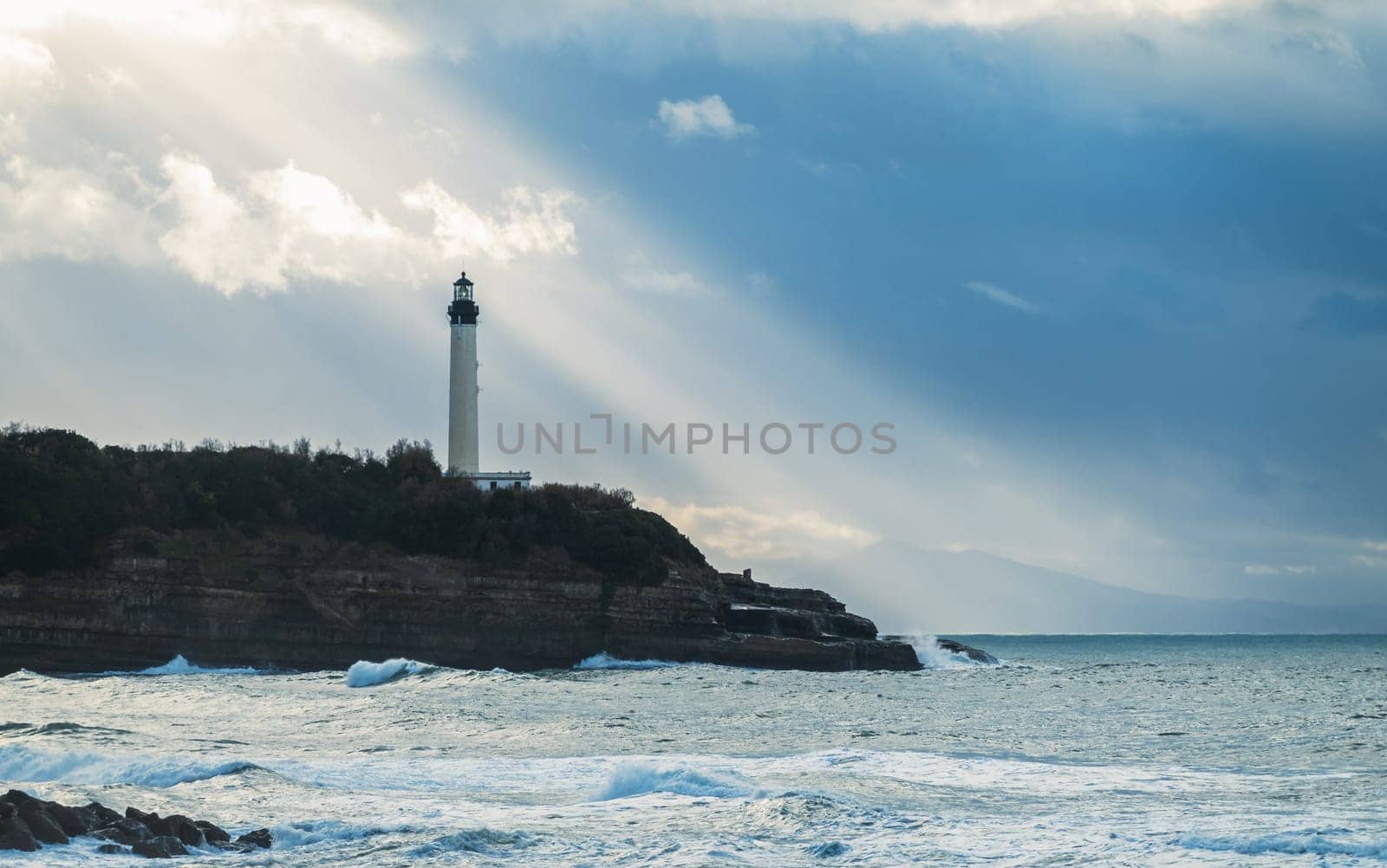 Biarritz lighthouse with sun rays in France, Atlantic Ocean in the foreground