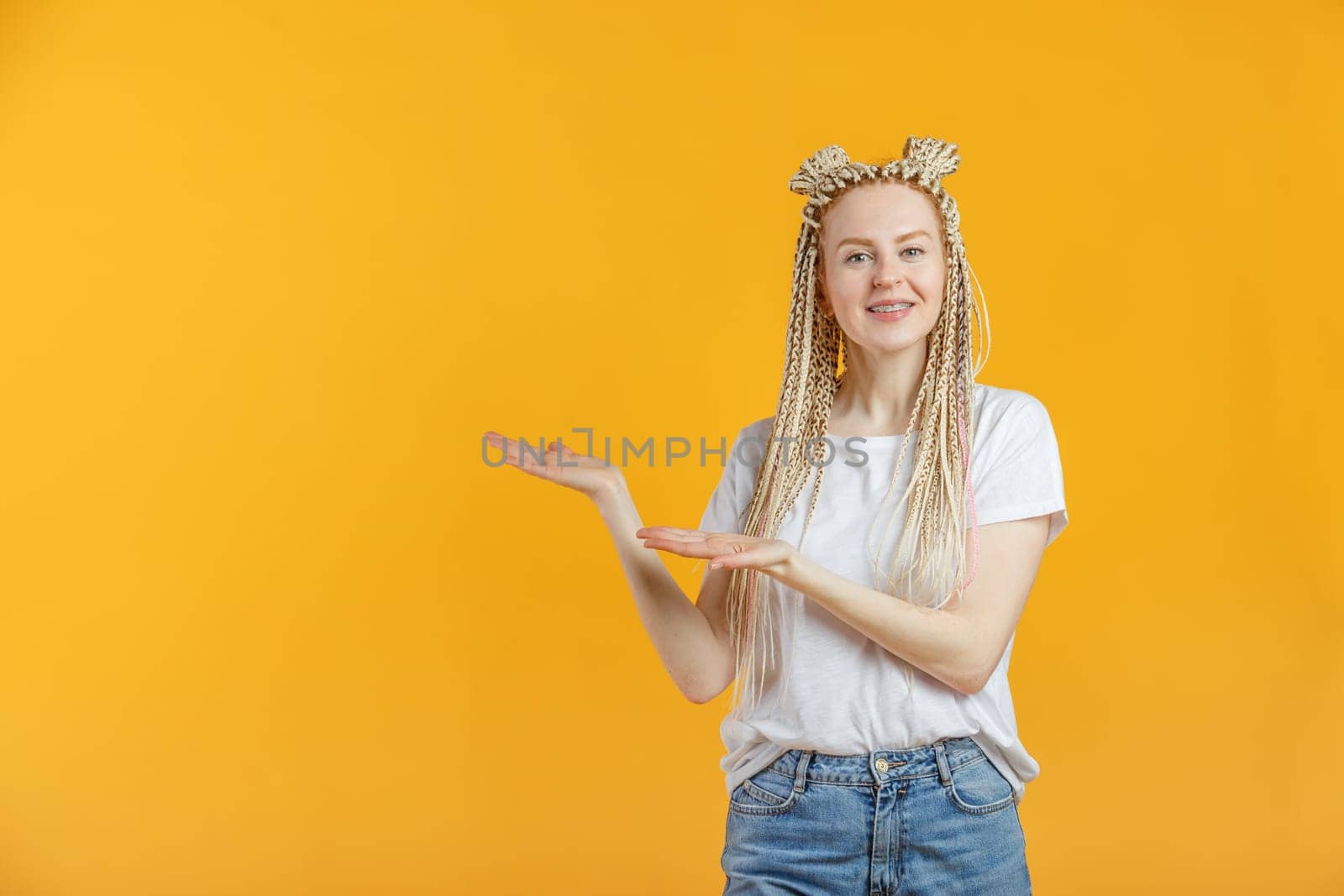 Smiling blonde caucasian woman in casual is pointing to empty space, isolated in yellow background.