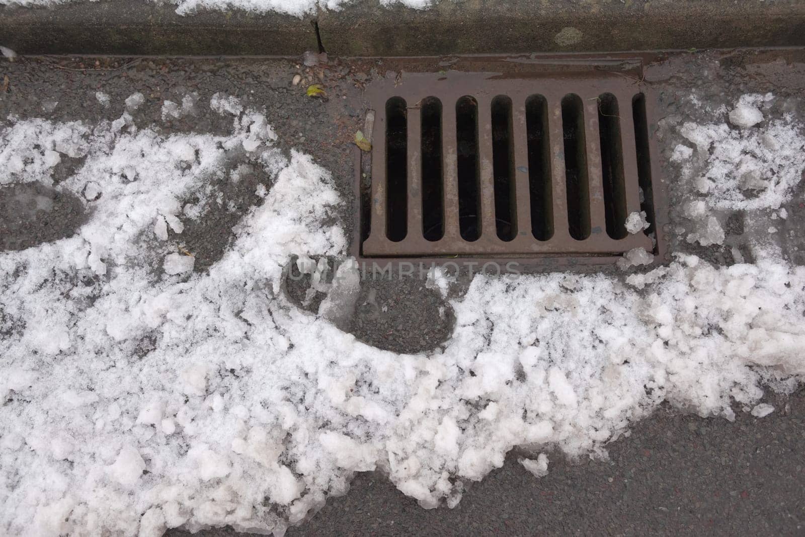 1 - Overhead view of a highway kerbside drain, also known as a surface drain, receiving water run off from melted snow. A Tarmac road in urban area.