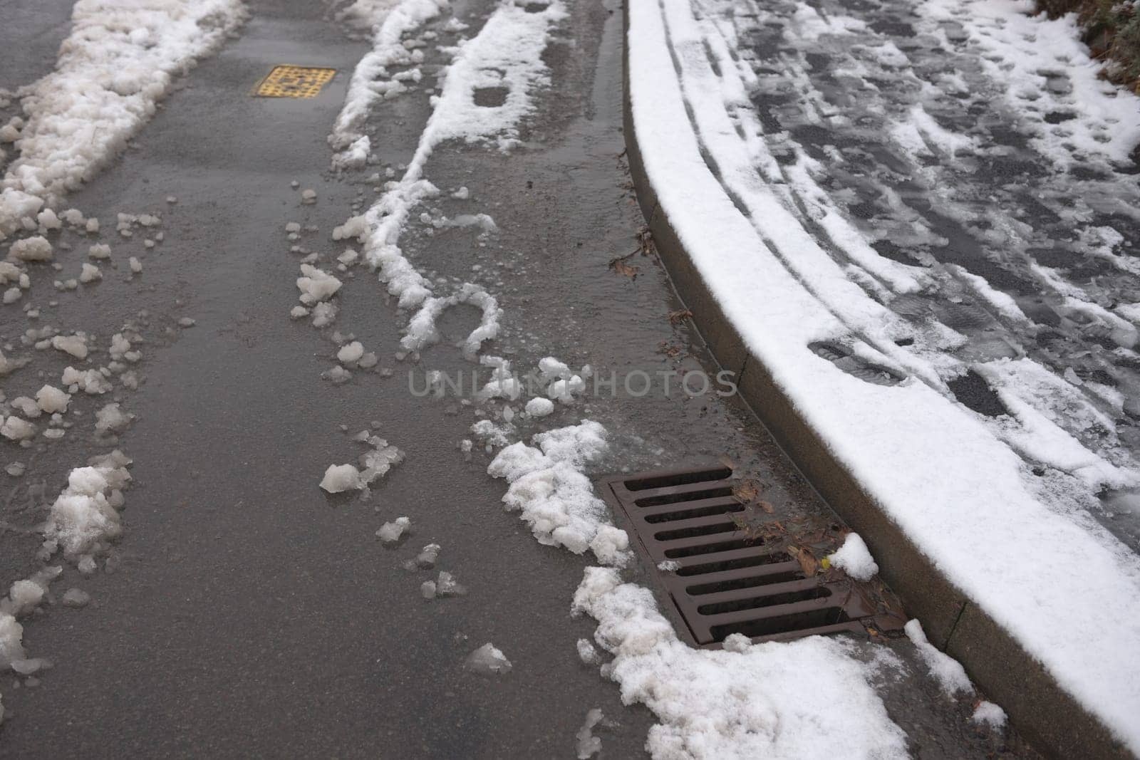 9 - Road and pavement covered in thawing snow. Road is partially cleared by cars, but sledge tracks and footsteps still line the pavement.