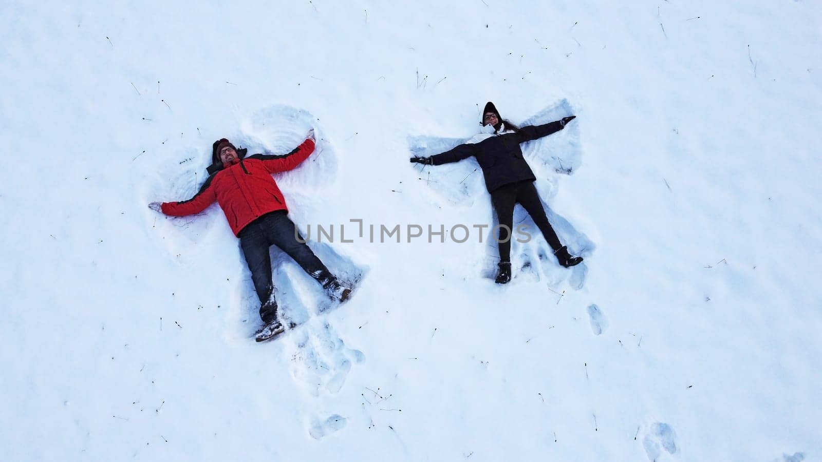 Drone shot of a woman and a man making a snow angel lying on the ground in winter