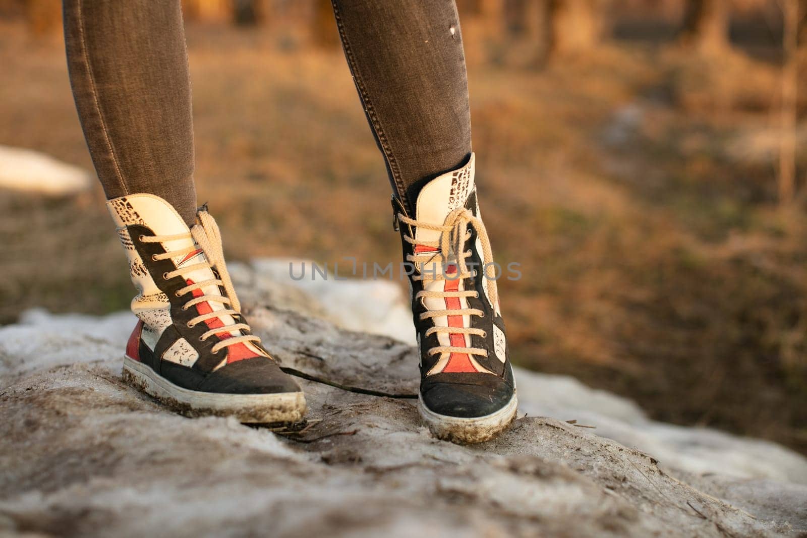Fashion sneakers women's high bright leather and white rubber boots worn with jeans and both feet facing forward.