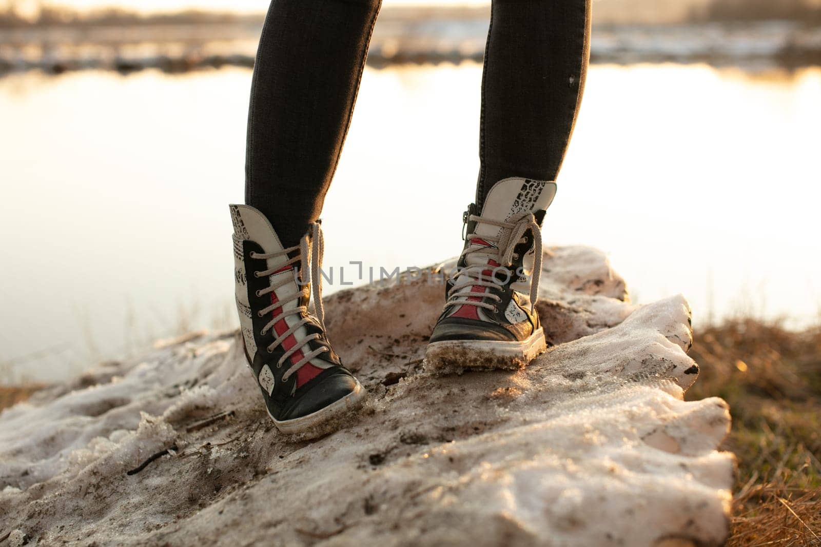 Fashion sneakers women's high bright leather and white rubber boots worn with jeans and both feet facing forward.