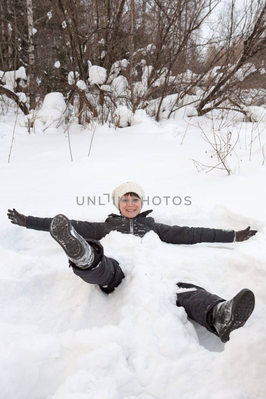 Side view of a beautiful young woman laying down on a frozen snow lake moving her arms up and down creating an angel figure shape, playing games while on vacation during a sunny winter day