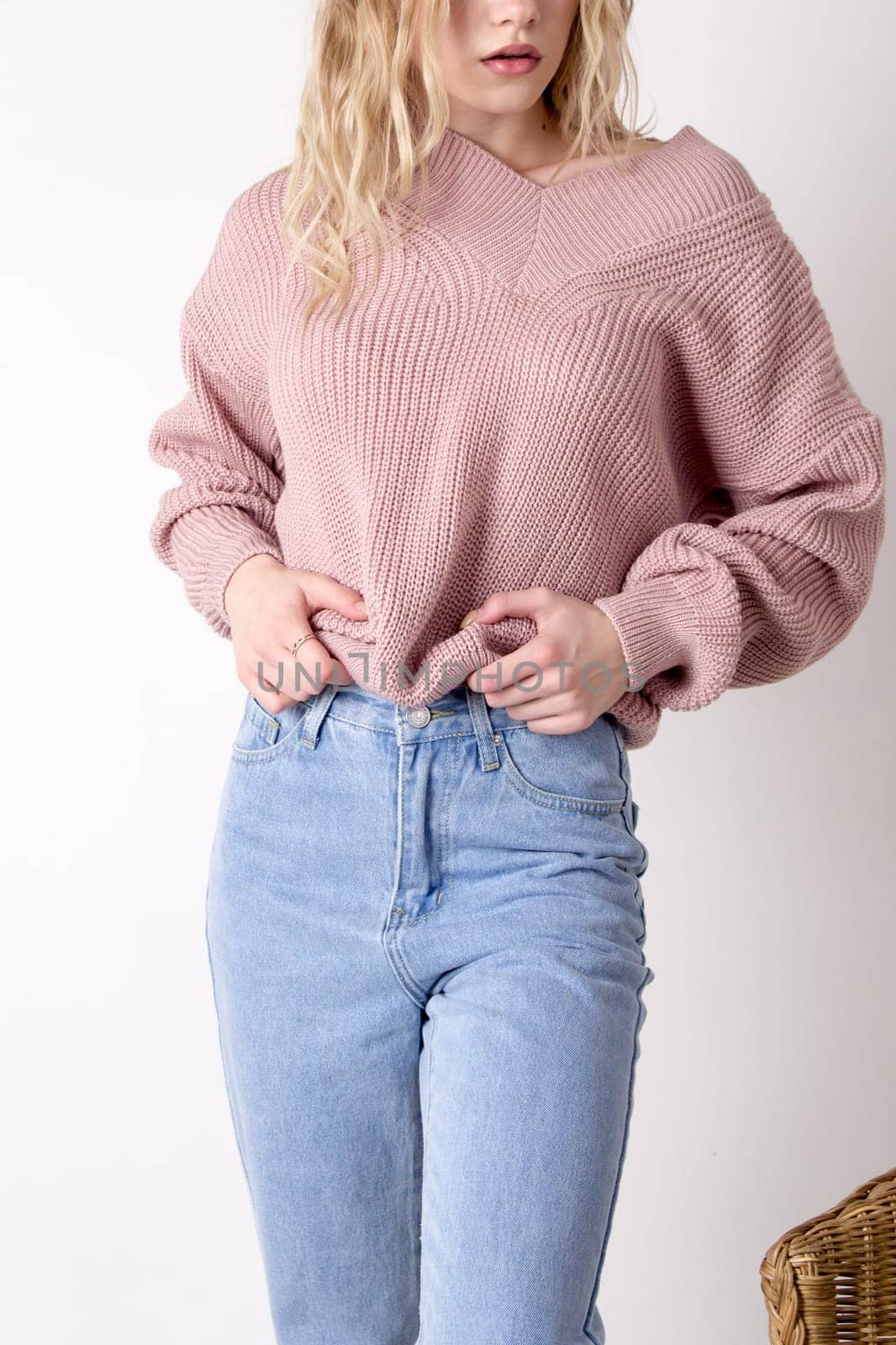 Photo of a teenage woman posing in high-waisted blue jeans and a sweater. Details of women's clothing