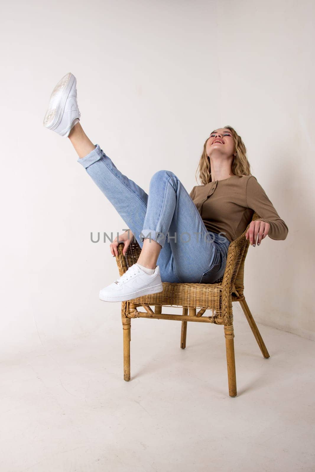 portrait of a beautiful young woman in jeans, shirt and sneakers.she put her feet up on the wicker rocking chair against the white brick wall.sitting on a chair.