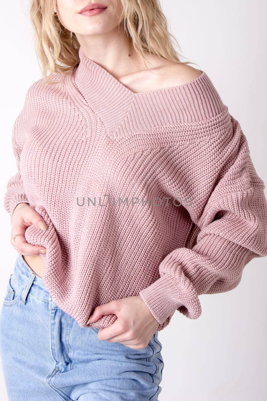 Photo of a teenage woman posing in high-waisted blue jeans and a sweater. Details of women's clothing