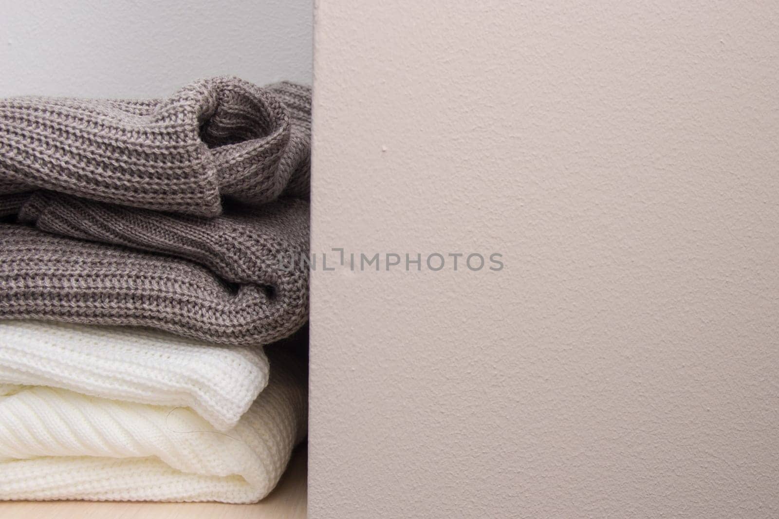 A stack of wool sweaters on the shelf. Grey and white sweater. Warm and cozy. Knitted clothing.