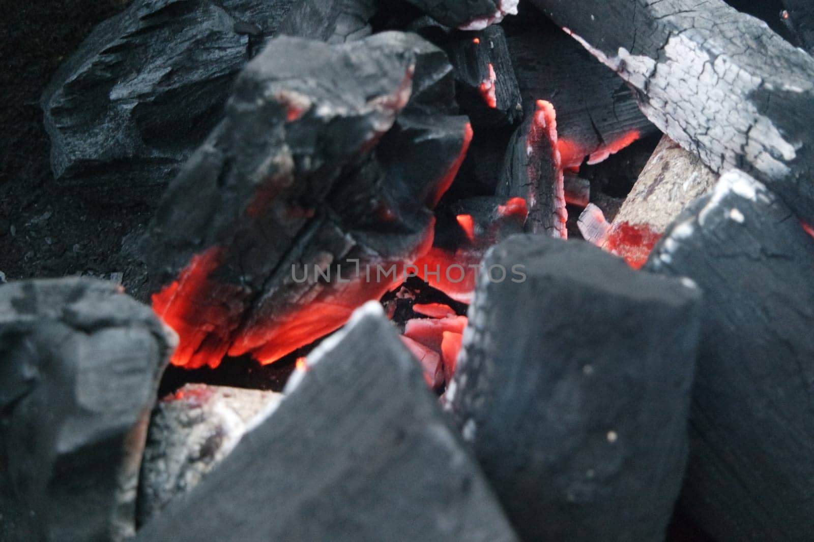 Fire on logs in fire pot with embers and burning coal. Bonfire with blazing red and orange fire flames. Fire background with woods and planks on fire at night view.