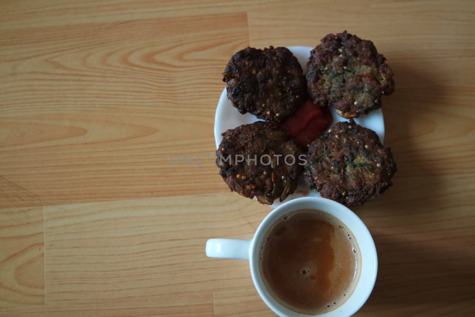 Delicious spicy fried round kebab served in white ceramic plate on a wooden floor with cup of hot tea.