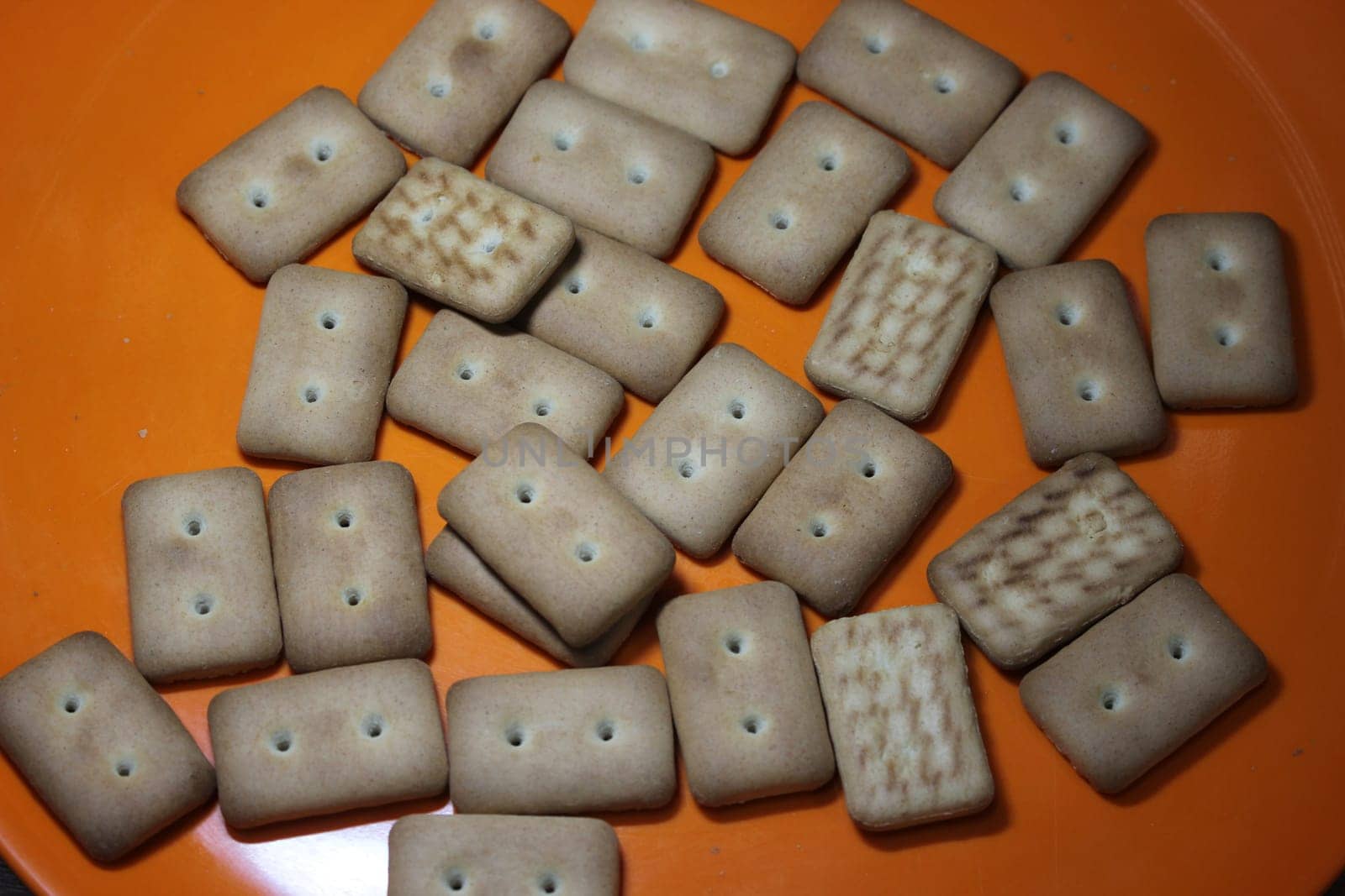 Close up top view of of biscuit cookies. Many rectangular biscuits with small pores in red plate