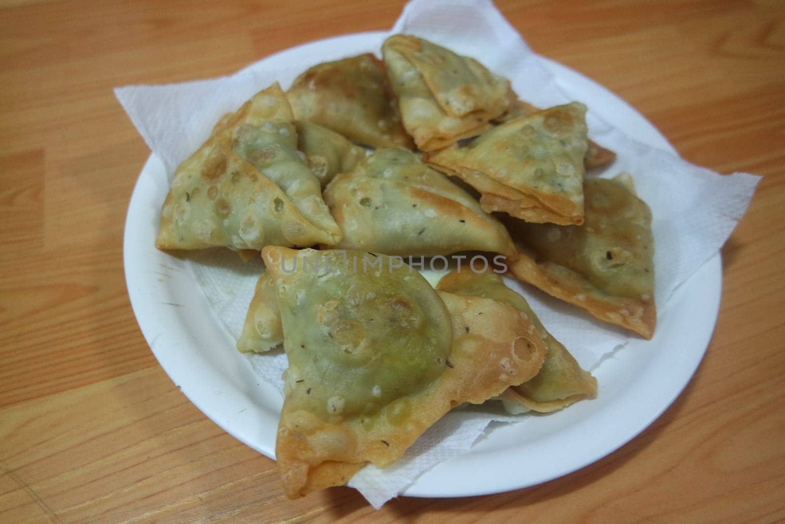 Closeup of delicious home made spicy and crunchy samosa pastries placed in a white ceramic plate on wooden floor