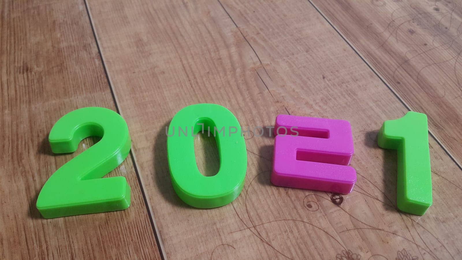 Plastic colored alphabets making words 2021 are placed on a wooden floor. These plastic letters can be used for teaching kids.
