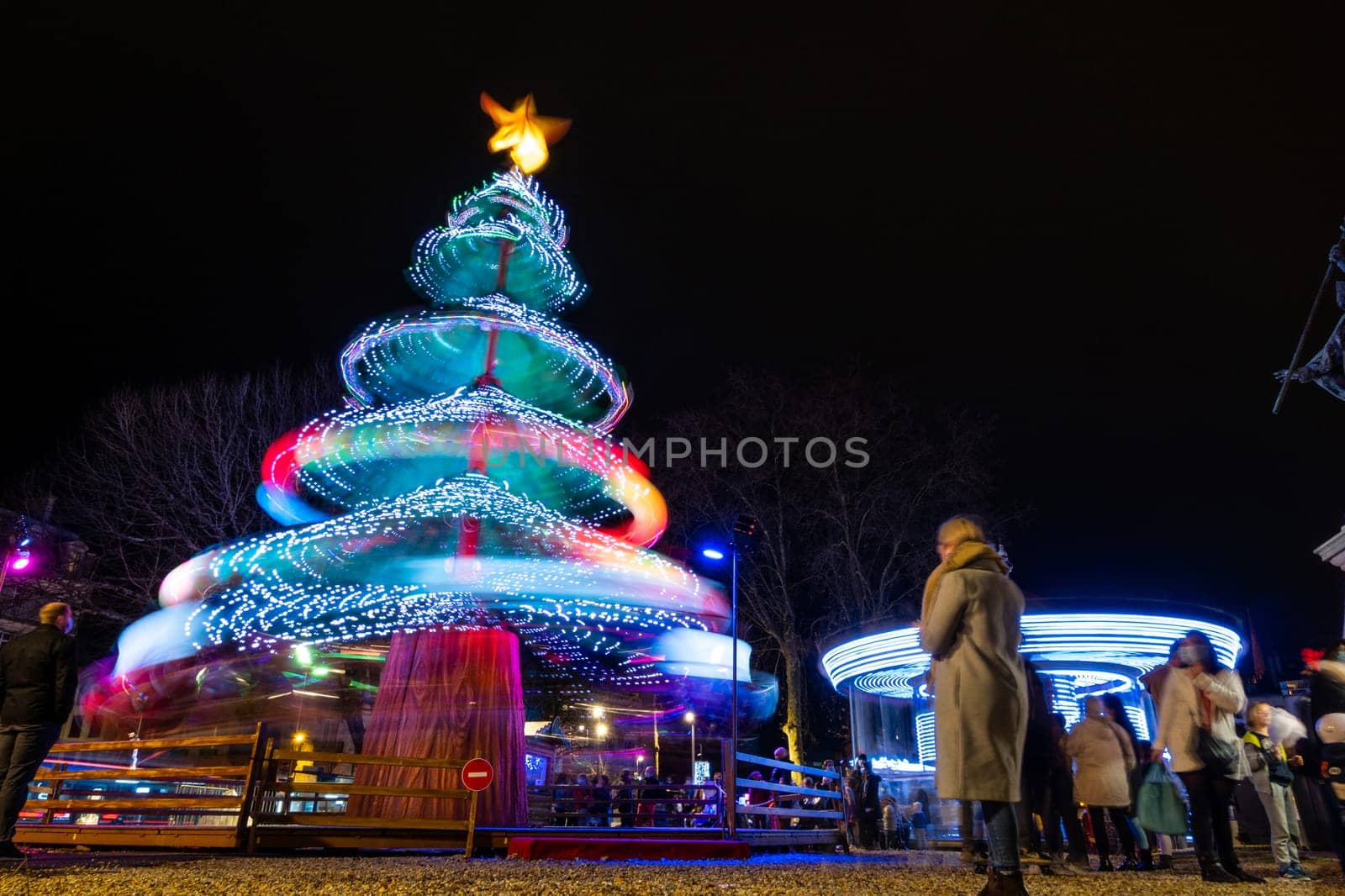 BAYONNE, FRANCE - CIRCA DECEMBER 2020: Long exposure of a Christmas tree carousel and a merry-go-round at night. Low angle shot with motion blur.