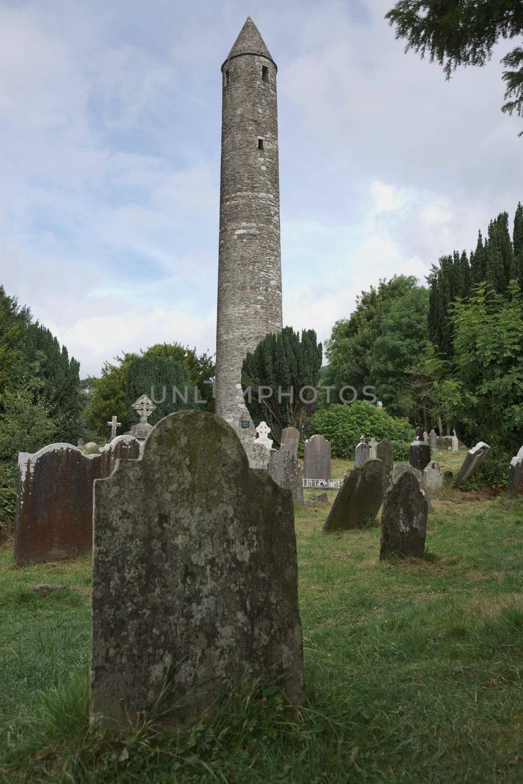 Glendalough, co. Wicklow, Ireland - August 10 2019 :Stone round tower and some ruins of a monastic settlement originally built in the 6th century in Glendalough valley, County Wicklow, Ireland.