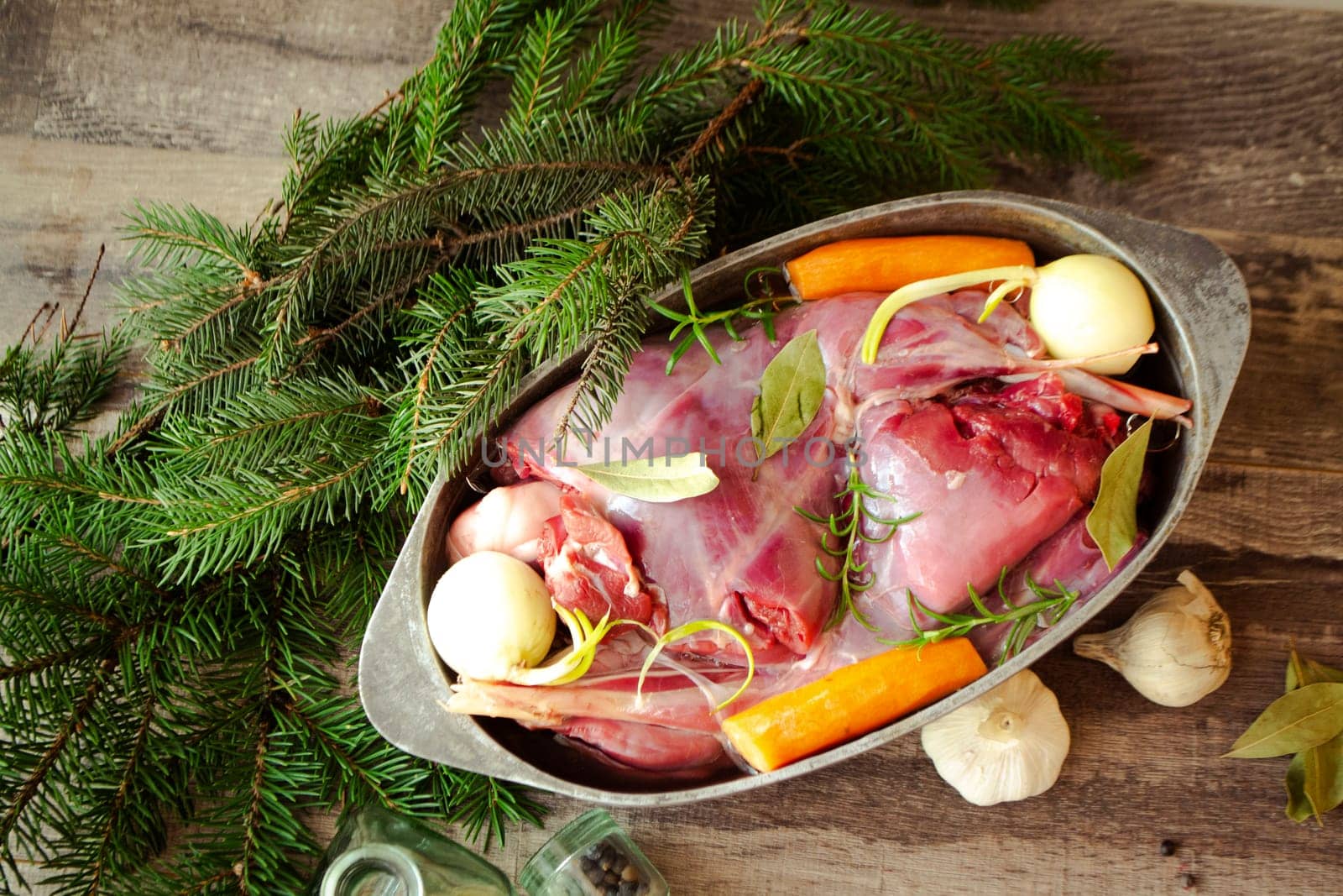 Roasted wild rabbit haunch with stewed vegetables in pan garnished with fresh herbs, flat lay