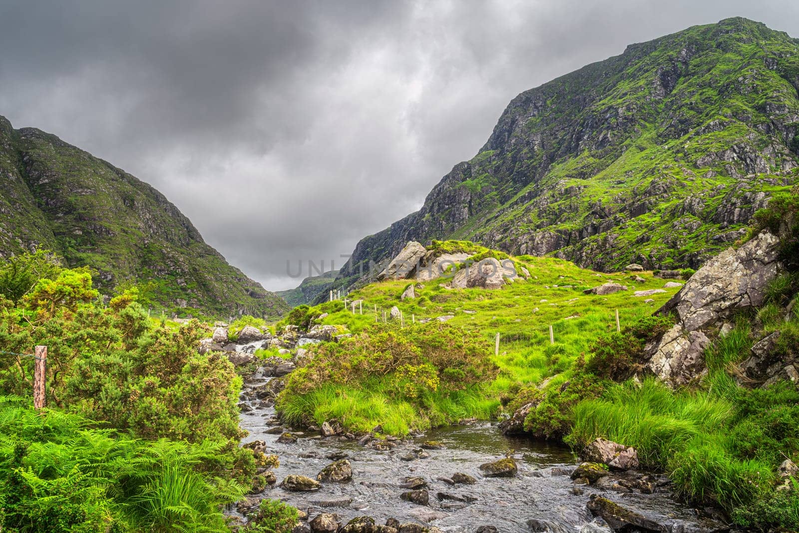 Small stream in beautiful green mountain valley, Gap of Dunloe, going between steep hills in Black Valley, County Kerry, Ireland