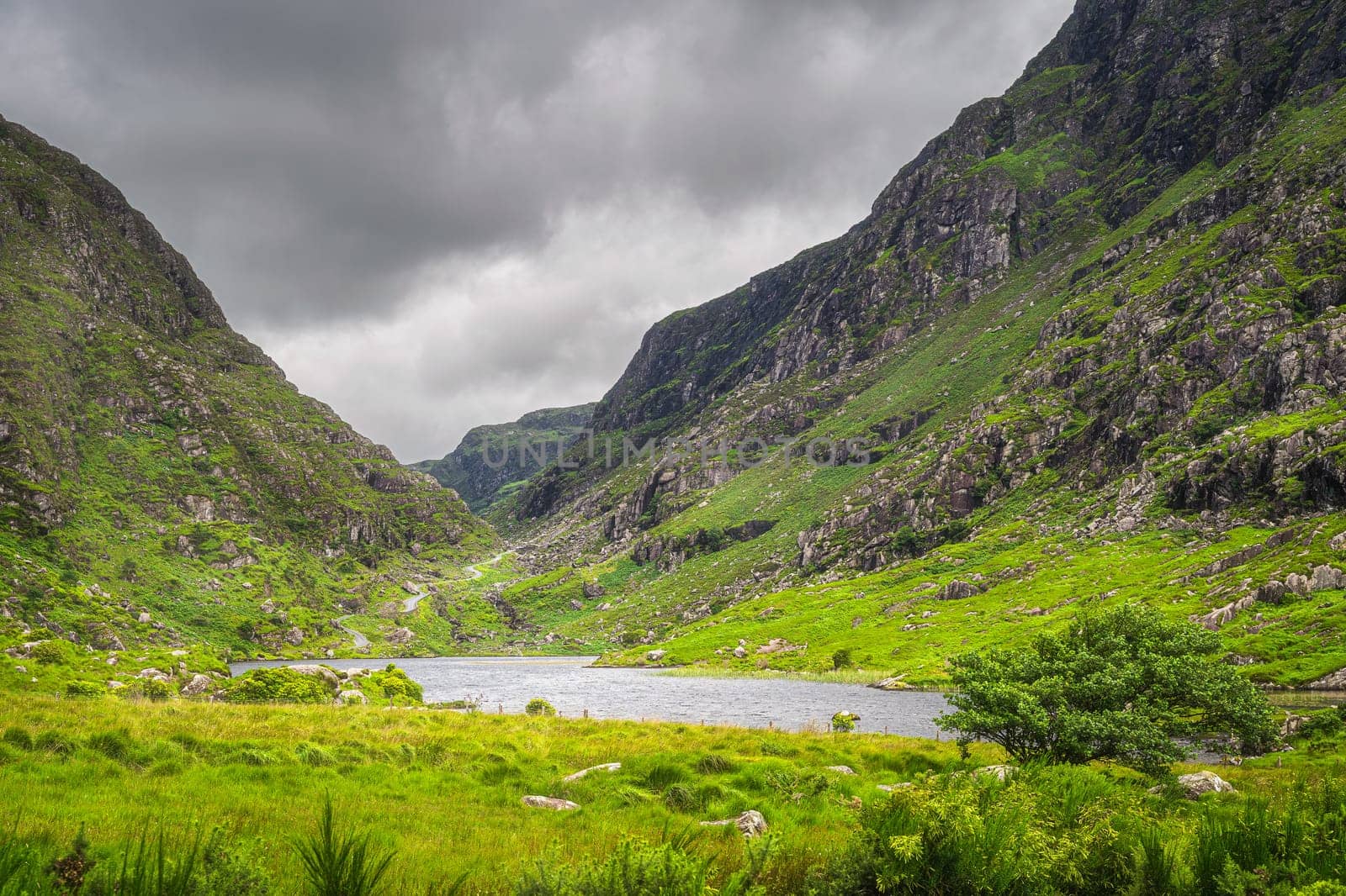 Small lake in beautiful green mountain valley, Gap of Dunloe, with winding road going between steep hills in Black Valley, County Kerry, Ireland
