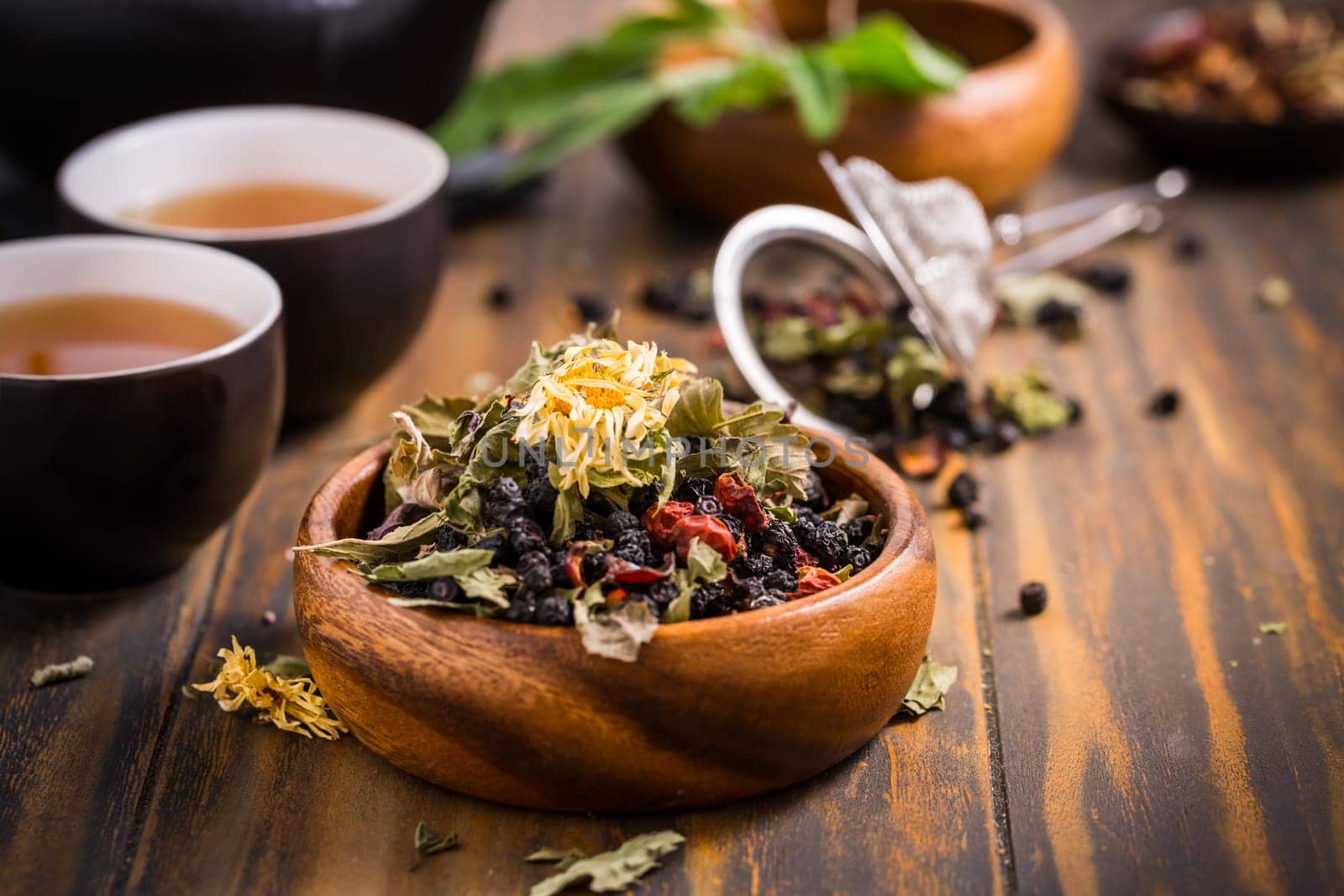Herbal and fruit tea concept with teapot and infuser and assorted herbal leaves on wooden background