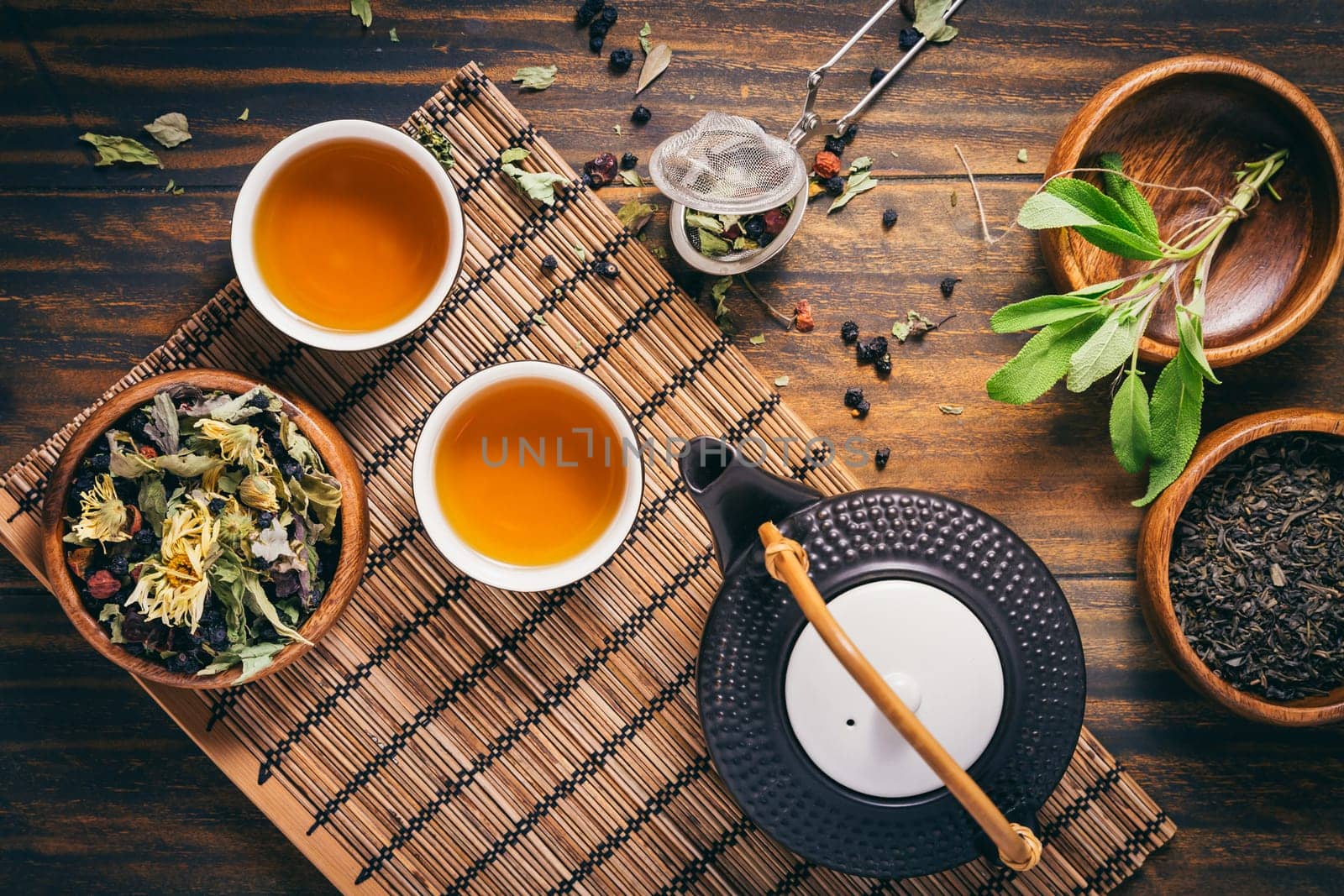 Herbal and fruit tea concept with teapot and infuser and assorted herbal leaves on wooden background