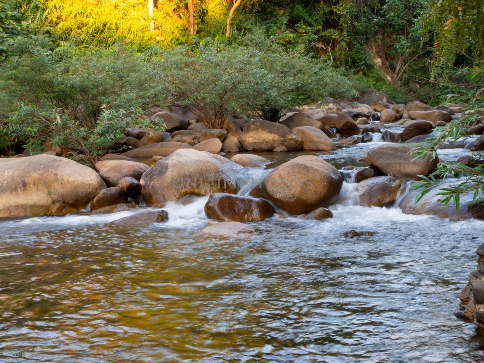A long-exposure shot of a small creek flowing through a brown rock. And there are green trees as a backdrop. It is a specific focus.