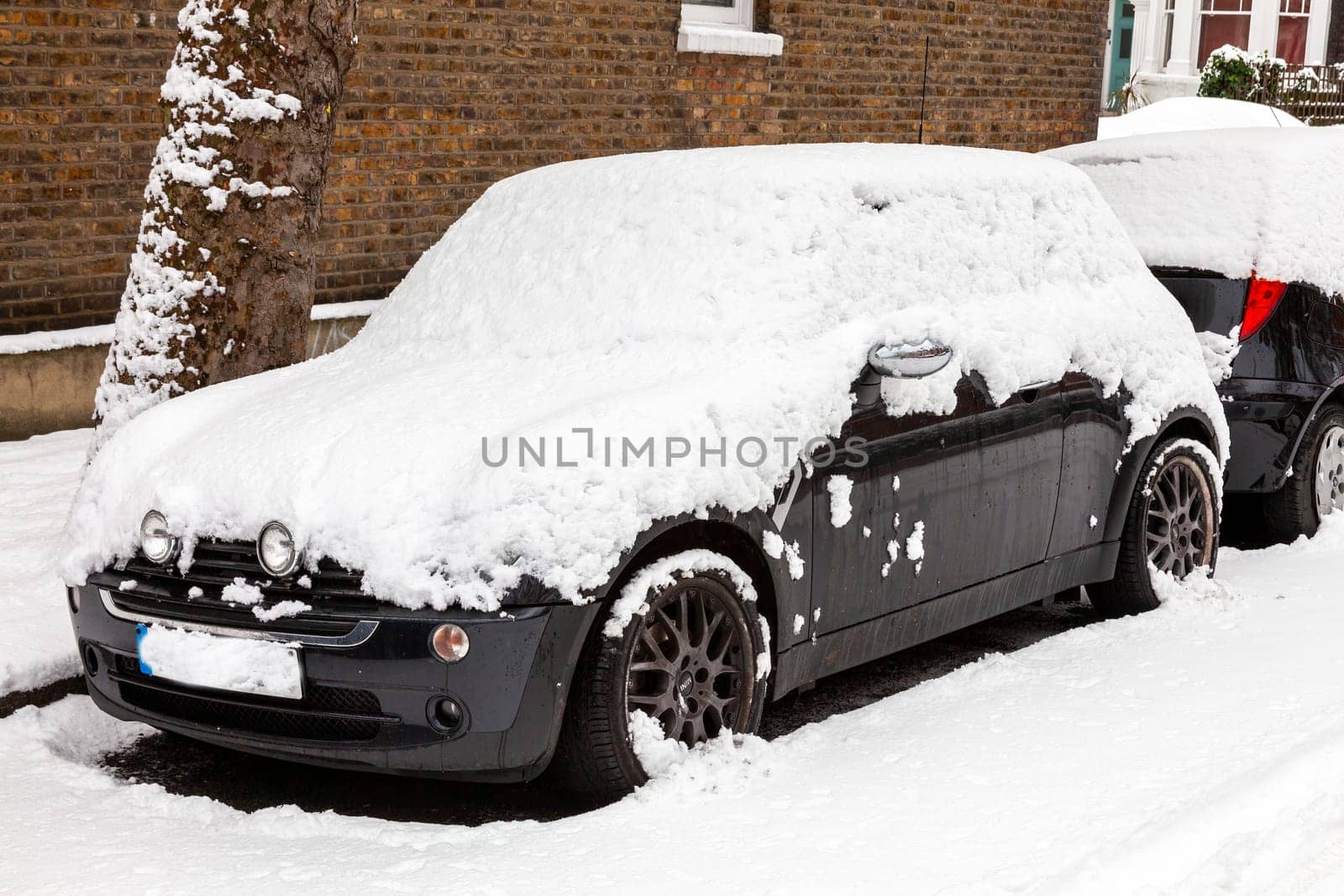 Street winter cityscape with snow covered frozen cars after a blizzard snowfall in London England UK, stock photo image