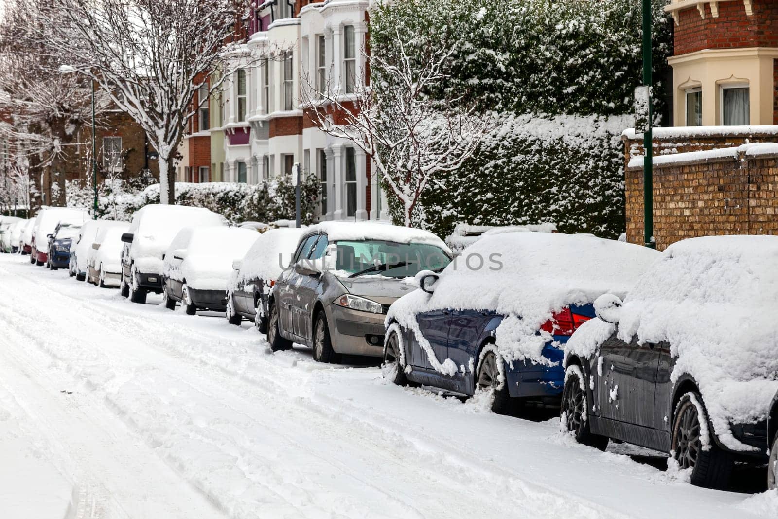 Street winter cityscape with snow terraced houses and frozen cars after a blizzard snowfall in London England UK, stock photo image with copy space